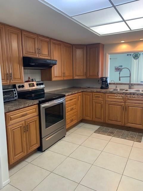 3013 Yarmouth Dr W, Bradenton, FL 34205 - kitchen with electric stove, under cabinet range hood, and brown cabinets