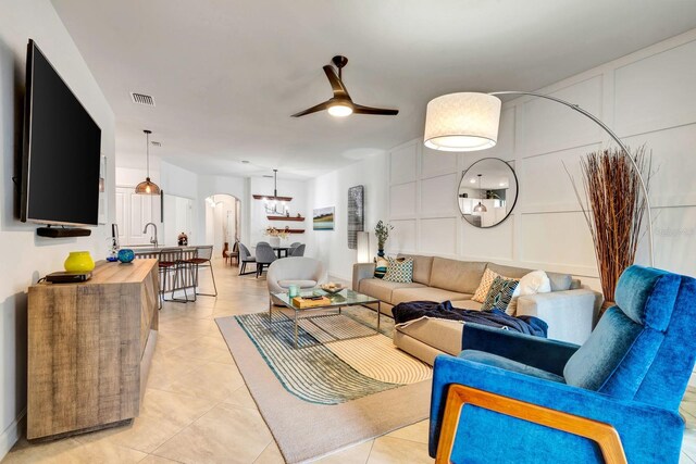 living area featuring ceiling fan, light tile patterned floors, arched walkways, a decorative wall, and visible vents