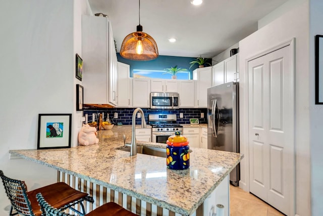 kitchen with light stone counters, stainless steel appliances, a peninsula, a sink, and decorative backsplash