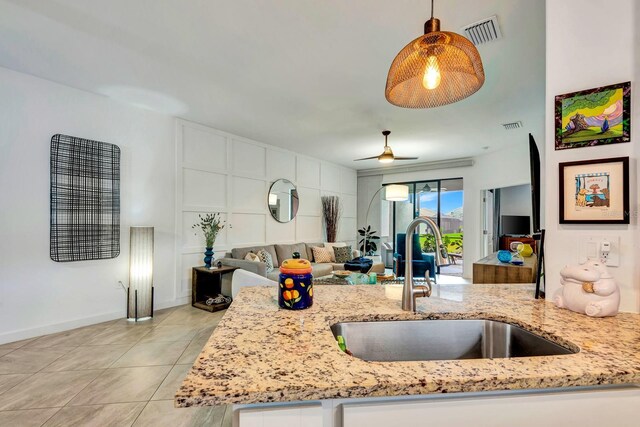 kitchen featuring light tile patterned floors, visible vents, light stone counters, open floor plan, and a sink