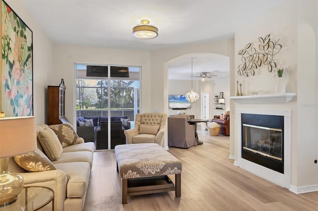 living room featuring ceiling fan, arched walkways, a glass covered fireplace, and light wood-style flooring