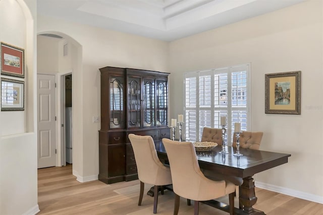 dining area featuring arched walkways, baseboards, a tray ceiling, and wood finished floors