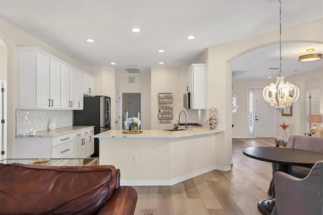 kitchen featuring a peninsula, light wood finished floors, white cabinets, and a sink