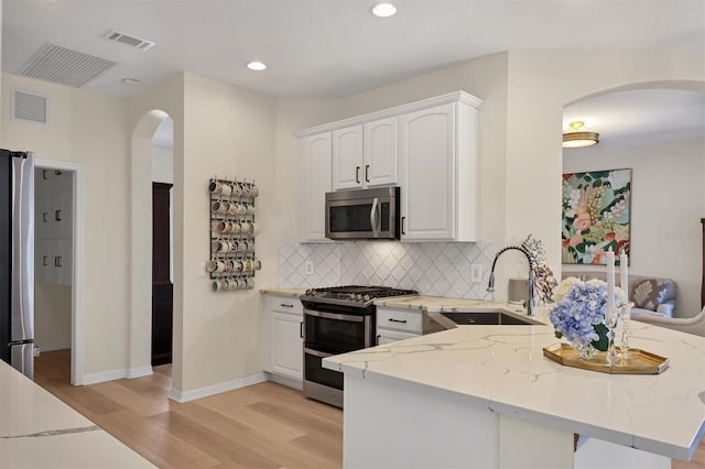 kitchen with visible vents, light stone counters, a peninsula, stainless steel appliances, and a sink