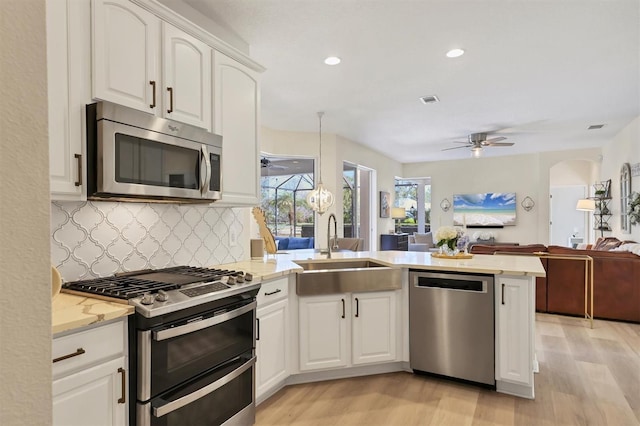 kitchen featuring arched walkways, appliances with stainless steel finishes, a ceiling fan, a sink, and a peninsula