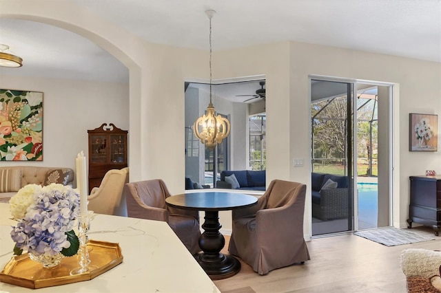 dining space featuring arched walkways, ceiling fan with notable chandelier, and wood finished floors