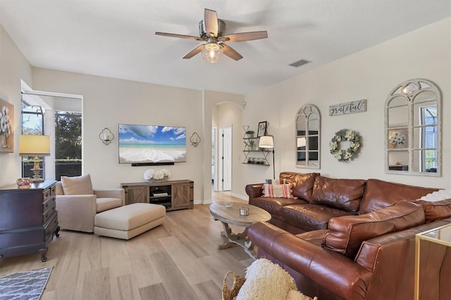 living area featuring visible vents, arched walkways, baseboards, light wood-style flooring, and ceiling fan