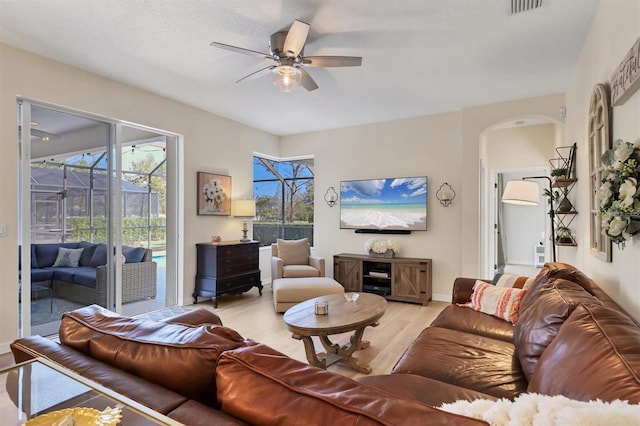 living room featuring visible vents, arched walkways, a sunroom, light wood-style flooring, and ceiling fan