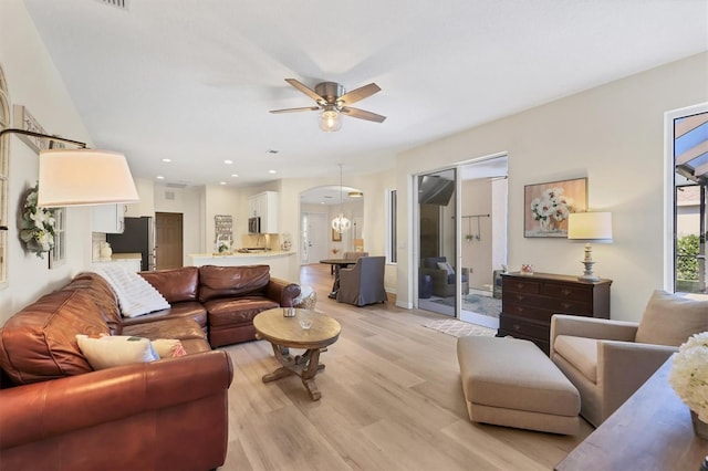 living room featuring ceiling fan with notable chandelier, light wood-style flooring, and recessed lighting