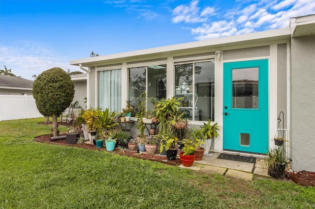 property entrance with a yard, fence, and stucco siding