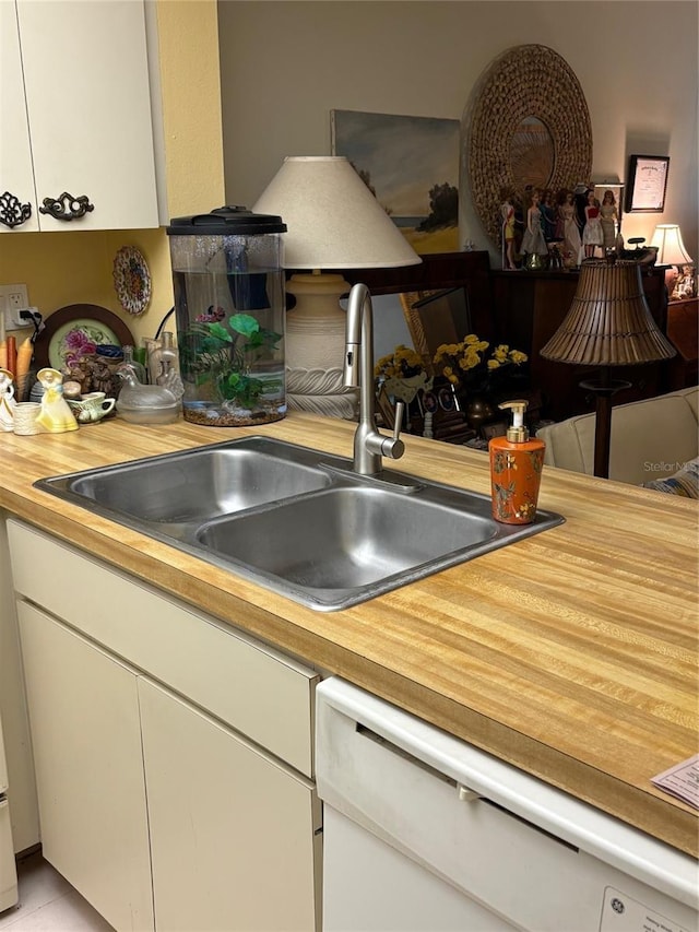 kitchen with white dishwasher, white cabinets, a sink, and butcher block countertops