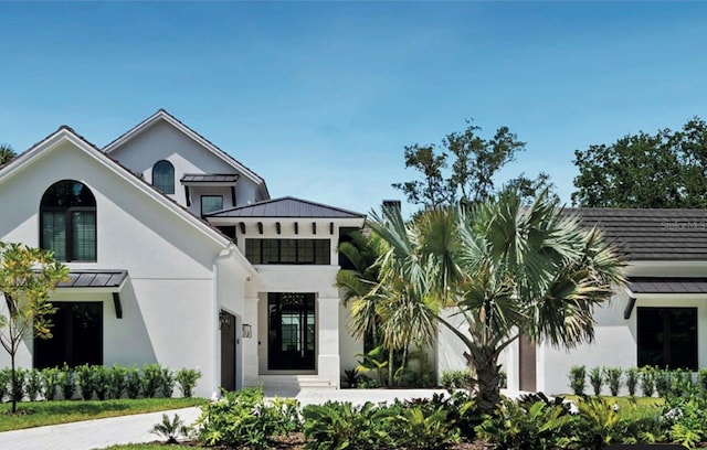 view of front facade featuring driveway, a standing seam roof, metal roof, and stucco siding