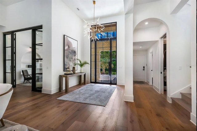 entrance foyer featuring arched walkways, stairway, a towering ceiling, wood finished floors, and baseboards