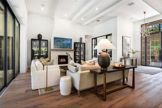 living room featuring beam ceiling, a fireplace, visible vents, a towering ceiling, and wood finished floors