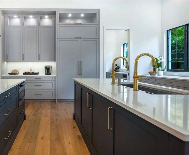 kitchen with light wood-style floors, glass insert cabinets, a wealth of natural light, and a sink