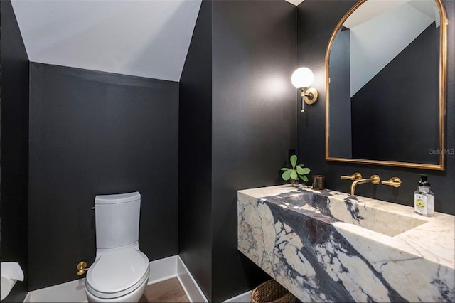 bathroom with vaulted ceiling, baseboards, a sink, and toilet