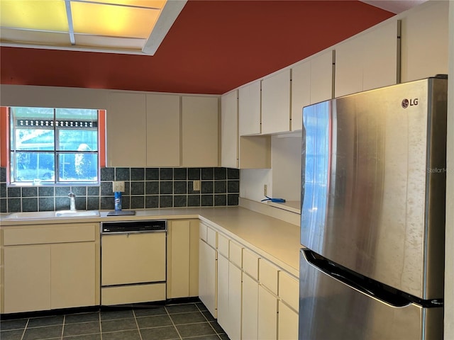 kitchen with dark tile patterned floors, a sink, light countertops, freestanding refrigerator, and dishwasher