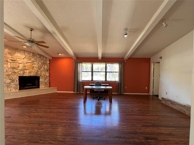 unfurnished living room featuring vaulted ceiling with beams, a stone fireplace, a textured ceiling, and wood finished floors