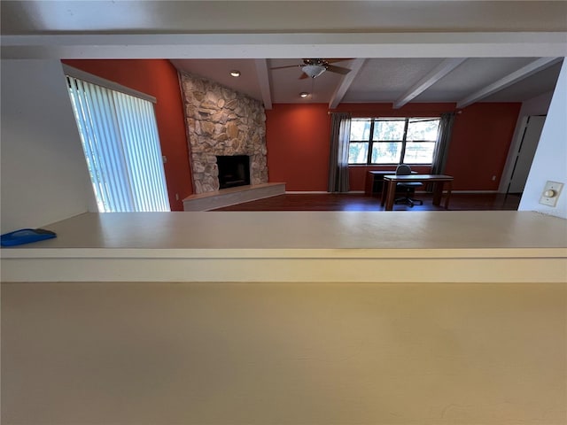 unfurnished living room featuring a fireplace, a ceiling fan, and beamed ceiling