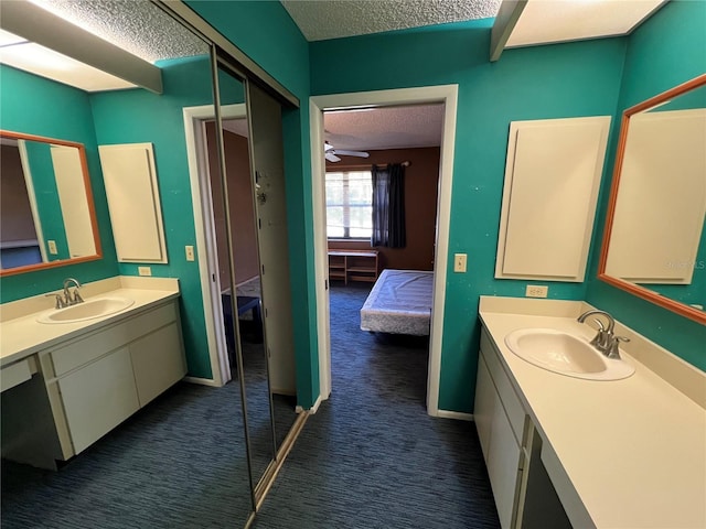 ensuite bathroom featuring a textured ceiling, ensuite bath, two vanities, and a sink