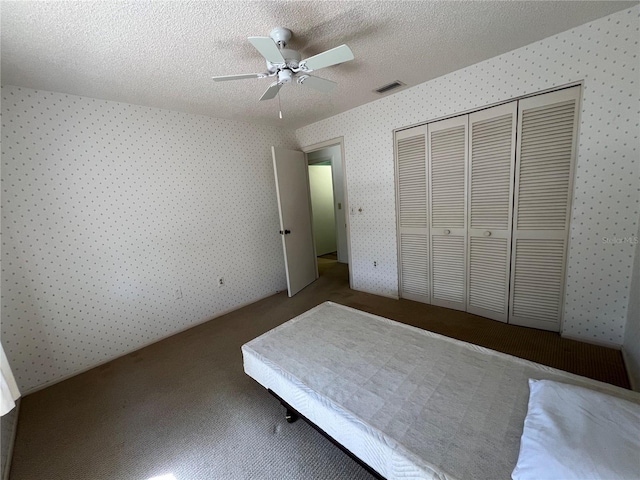 unfurnished bedroom featuring wallpapered walls, visible vents, ceiling fan, a textured ceiling, and a closet