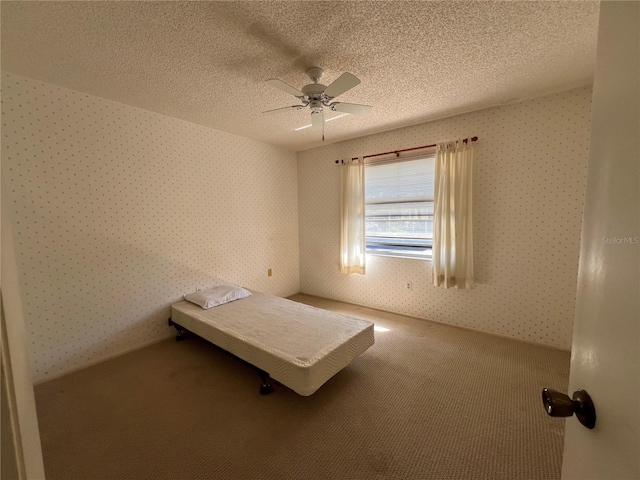 unfurnished bedroom featuring carpet floors, wallpapered walls, a ceiling fan, and a textured ceiling