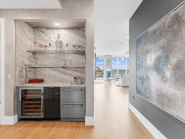 bar featuring beverage cooler, baseboards, a bar, floor to ceiling windows, and light wood-style floors