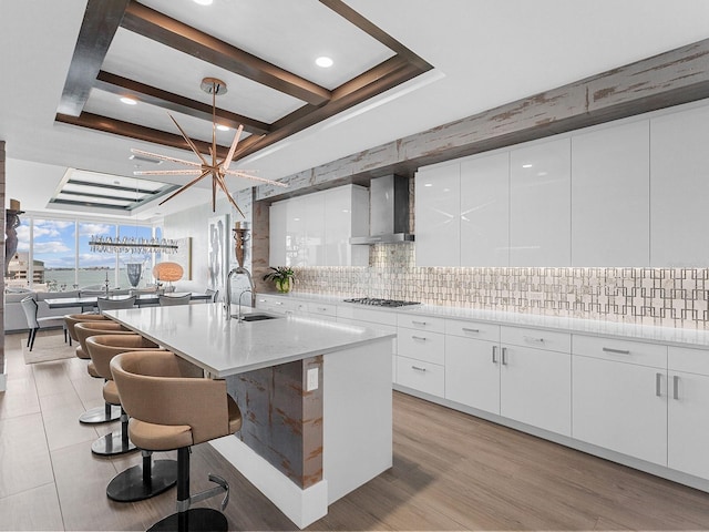 kitchen with tasteful backsplash, wall chimney range hood, gas stovetop, white cabinetry, and a sink