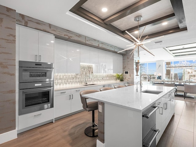 kitchen with white cabinets, a raised ceiling, a warming drawer, and a sink