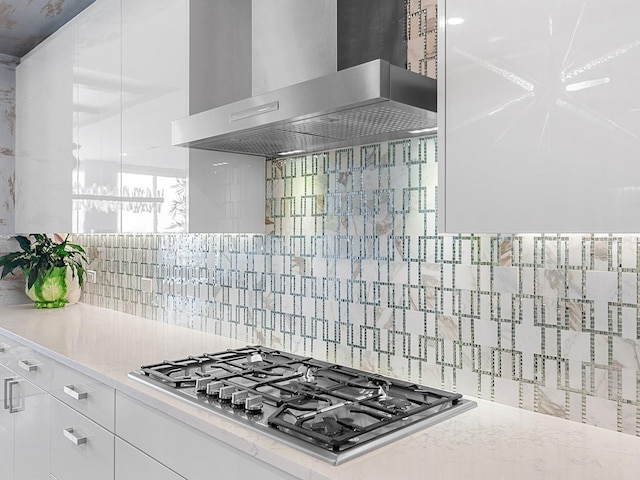 kitchen with light stone counters, decorative backsplash, stainless steel gas stovetop, white cabinetry, and wall chimney exhaust hood