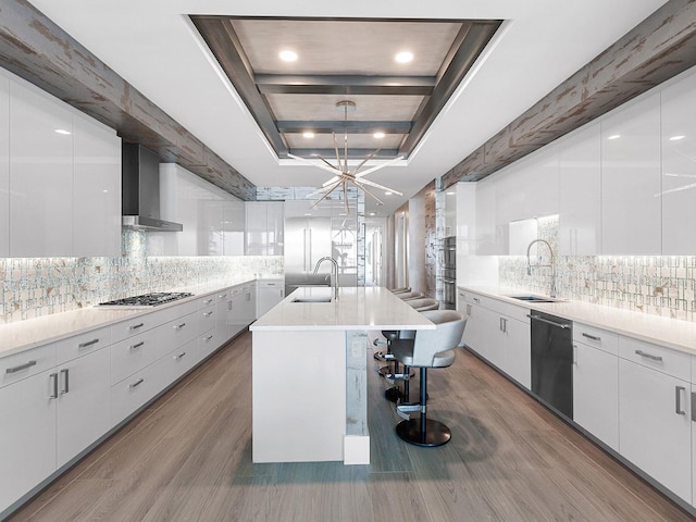 kitchen featuring wall chimney range hood, modern cabinets, stainless steel appliances, and a sink