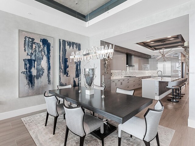 dining area with light wood-type flooring, a raised ceiling, and baseboards