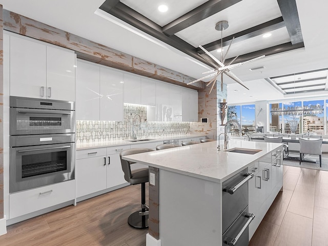 kitchen featuring a center island with sink, white cabinets, a warming drawer, and a sink