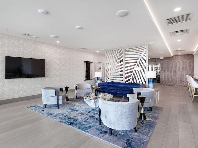 living area with visible vents, wood finished floors, and wallpapered walls