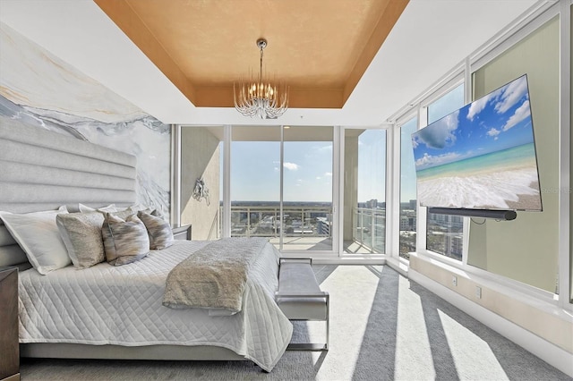 carpeted bedroom with a wall of windows, a raised ceiling, multiple windows, and a chandelier