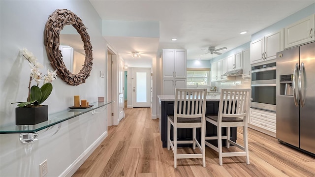 kitchen featuring backsplash, under cabinet range hood, light wood-type flooring, a kitchen breakfast bar, and stainless steel appliances