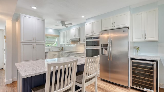 kitchen with white cabinets, beverage cooler, under cabinet range hood, and stainless steel appliances