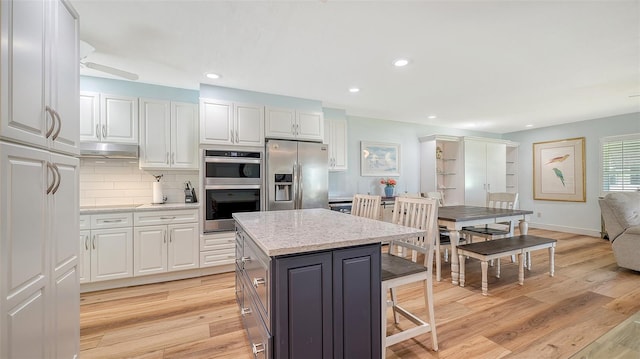 kitchen featuring a kitchen island, light wood-type flooring, decorative backsplash, appliances with stainless steel finishes, and white cabinetry