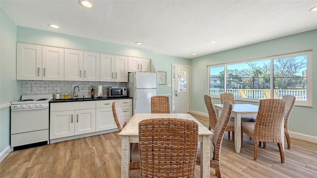 kitchen featuring white appliances, light wood-type flooring, backsplash, and a sink