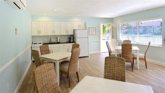 kitchen with light wood finished floors, decorative backsplash, white appliances, a wall mounted AC, and a sink