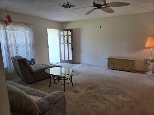 living room with a textured ceiling, carpet floors, visible vents, and a ceiling fan