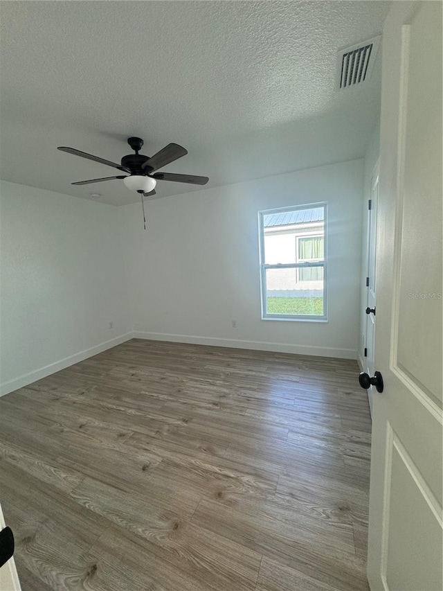 spare room with baseboards, visible vents, a ceiling fan, wood finished floors, and a textured ceiling