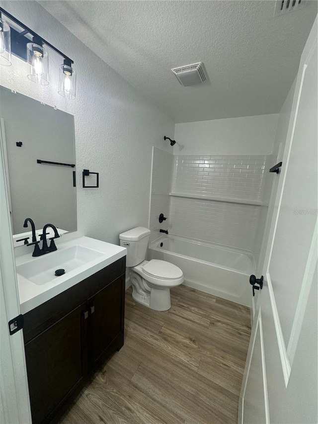 bathroom featuring visible vents, toilet, wood finished floors, a textured ceiling, and shower / washtub combination