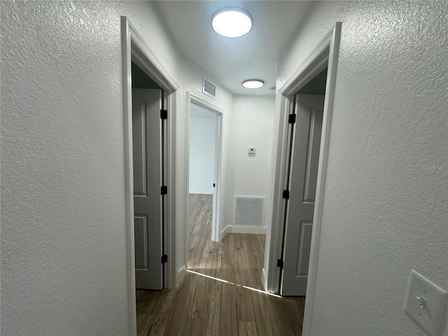 corridor with a textured wall, dark wood-style flooring, and visible vents