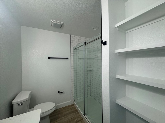 full bath featuring visible vents, toilet, wood finished floors, a textured ceiling, and a shower stall