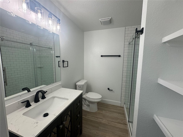 full bath with toilet, wood finished floors, a textured ceiling, vanity, and a shower stall