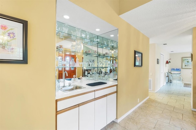 bar featuring visible vents, a sink, a textured ceiling, wet bar, and baseboards