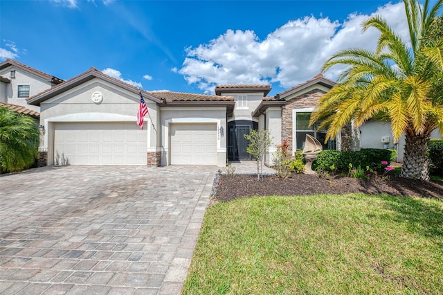 mediterranean / spanish-style home featuring a garage, a tile roof, stone siding, decorative driveway, and stucco siding