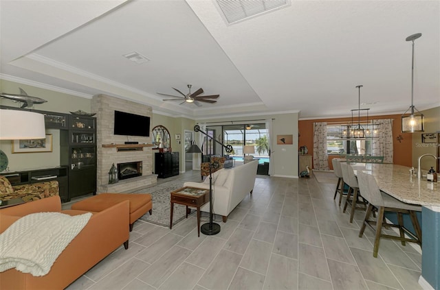 living room featuring a large fireplace, visible vents, a raised ceiling, and ceiling fan with notable chandelier