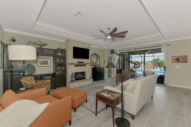 living room with a tray ceiling, a fireplace, visible vents, a sunroom, and light tile patterned flooring